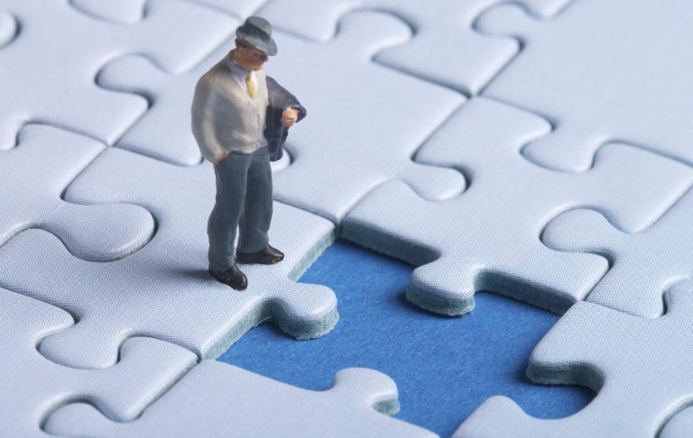 Eine kleine männliche Figur steht vor einem Puzzle, wo ein Puzzleteil fehlt. 